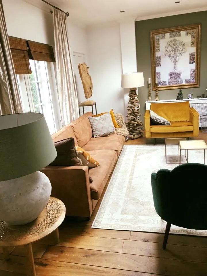 Een zitgedeelte in het pand, met een leren bank, een groene fauteuil en een olijfgroene wand.